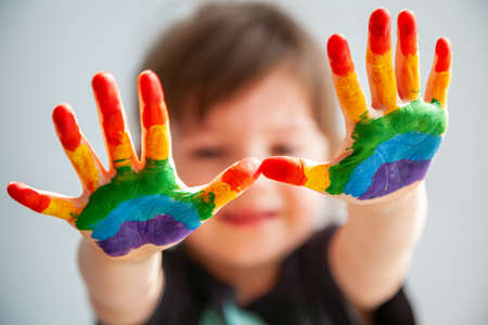 Cute little girl showing her hands with rainbow painted on her palmsの写真素材