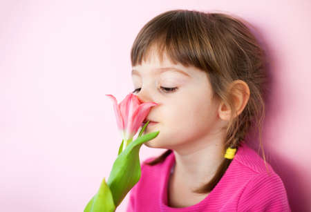 Cute little girl in pink dress sniffing a pink tulip on a pink backgroundの写真素材