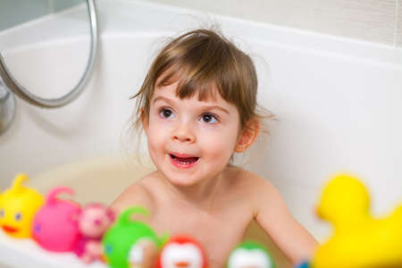 Bath time. Cute little girl taking a bath and playing with her toys while sitting in a bathtub