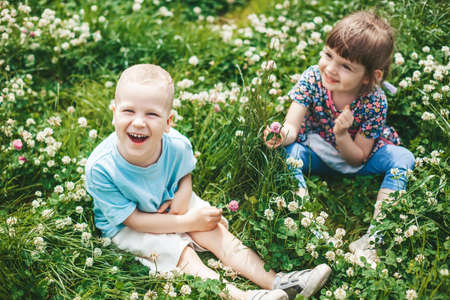 Two happy children friends, a boy and a girl, sitting on a clover field, having fun togetherの写真素材
