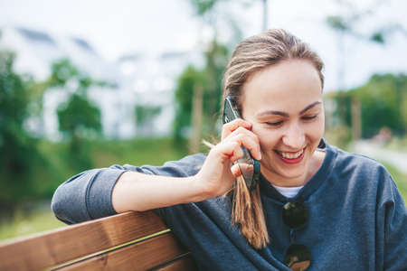 Candid young woman talking by phone, sitting on a bench outside