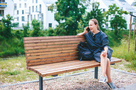 Candid young woman talking by phone, sitting on a bench outsideの写真素材