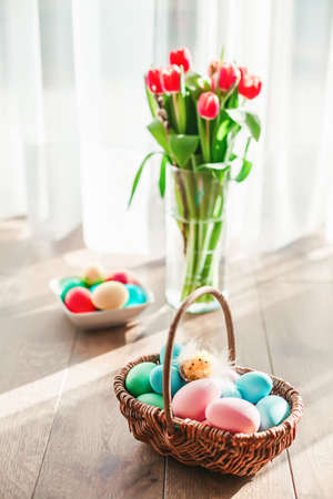 Pastel colored Easter eggs in a basket with tulips on a background