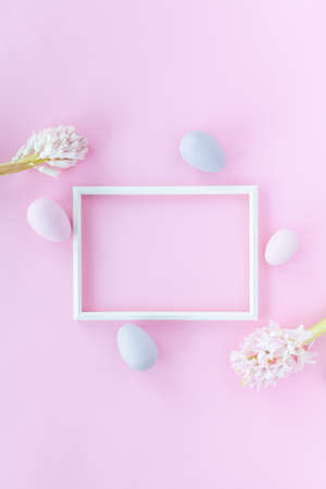 Minimalistic Easter background with pastel colored eggs, photo frame and hyacinth flowers on a pink background. Flat lay greeting card with space for text.の写真素材
