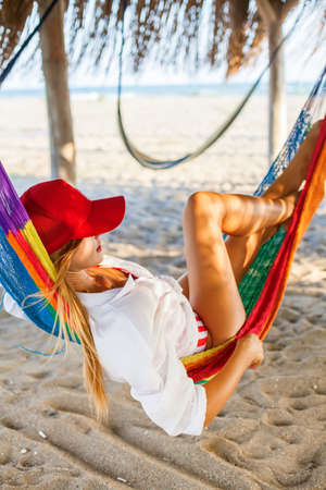Blonde woman in red cap relaxing in a hammock on a beachの写真素材