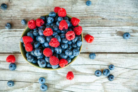 Top view fresh ripe blueberry and raspberry in a bowl on a wooden background