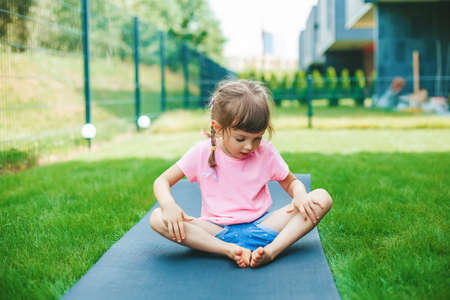 Cute little girl 4-5 years old sitting in the Butterfly position while practicing yoga outdoors....