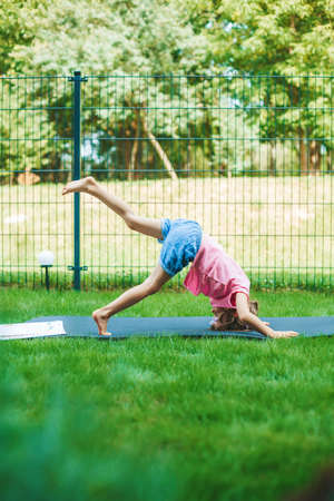 Little girl stretching on the roll mat practicing yoga in the park outdoor. Yoga for children. Kid's healthy lifestyle.の写真素材
