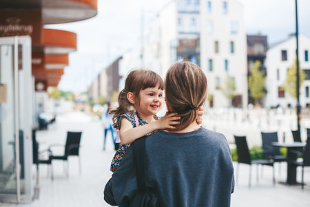 Woman carrying her cute little daughter and they are hugging each other, while walking on the streetの写真素材