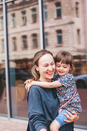 Young woman carrying her cute little daughter and they are hugging each other, while walking on the streetの写真素材