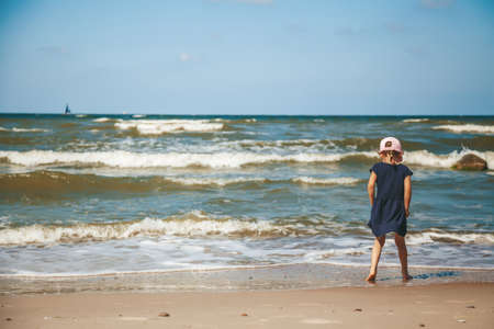 Little girl standing alone watching the waves on the beach of a Baltic sea