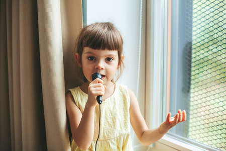 Cute little girl with microphone singing at homeの写真素材