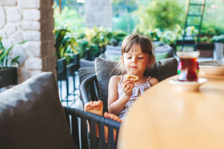 Cute little girl sitting at the cafe and eating onion rings