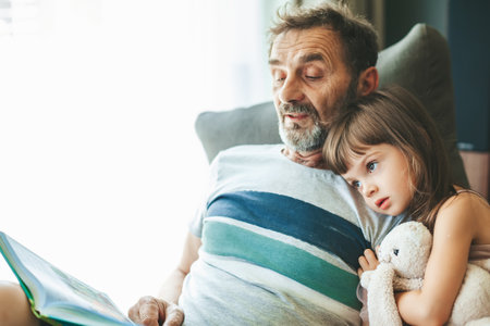 Grandfather reading a book to his granddaughter, sitting on a bean bag chair. Grandpa telling...
