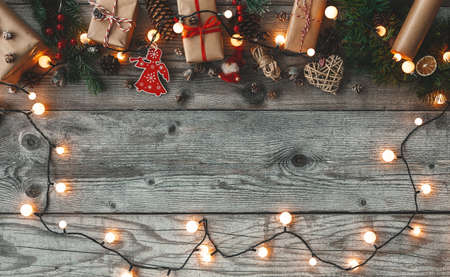 Flat lay Christmas composition with handcraft gift boxes, light bulbs garland, pine cones and decorations on a rustic wooden background. Top view, copy-space. Merry christmas and happy New Year!の写真素材