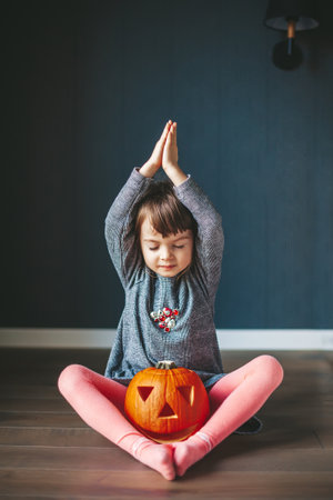 Cute little girl with closed eyes and with a Halloween Jack pumpkin, sitting in a lotus positionの写真素材