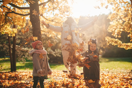 Mother with two kids throwing autumn leaves, playing in the autumn park. Autumn leaf fall. Family having fun together.の写真素材