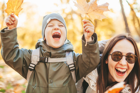 Laughing mother with her little son playing with autumn leaves. Family having fun together outside during autumn season.の写真素材