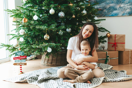 Happy smiling mother and her little son sitting on the floor near the decorated Christmas tree at home. New Year's holidays with family.の写真素材