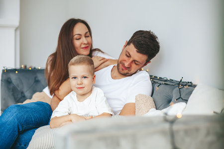 Portrait of a cute little boy sitting on a soft gray couch with his young parentsの写真素材