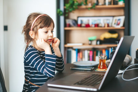 Little girl 4-5 years old using laptop. Kid having a video call or watching cartoons or having an...