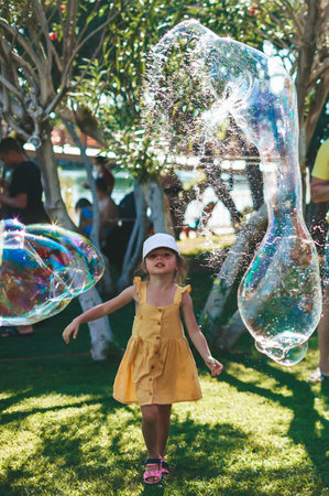 Cute little girl playing with very big soap bubbles. Summer outdoor activities.