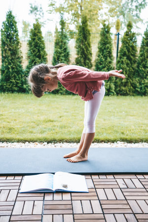 Little girl bending over while practicing yoga outdoors. Yoga for children. Kid's healthy lifestyle.の写真素材