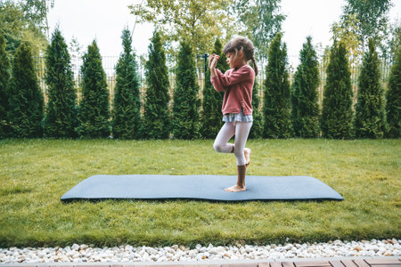 Cute little girl 5-6 years old standing in the Eagle position or Garudasana while practicing yoga outdoors. Yoga for children concept.の写真素材