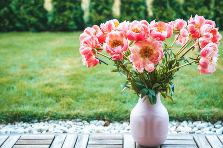 A bouquet of vibrant pink peonies with copy-space. These flowers are housed in a pink, ribbed vase,...
