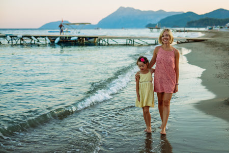 A young girl and her mother hugging and walking along the beach, close to the water's edge, in the peaceful light of late afternoonの写真素材