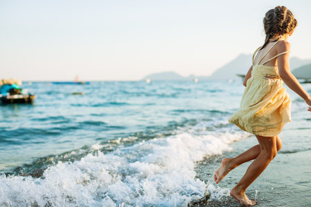 Little girl running away from the waves on the beach, capturing a serene moment of relaxation and childhood joy by the waterの写真素材