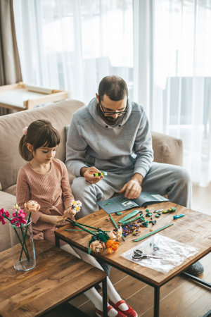 In a well-lit living room, a father and his 5-6 year old daughter are crafting with small construction pieces at a wooden tableの写真素材