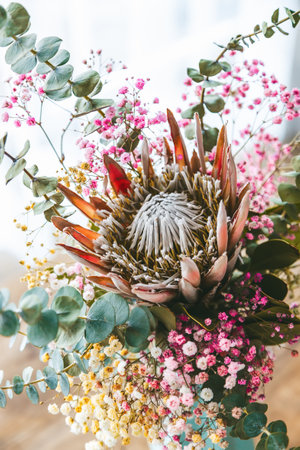 Close-up beautiful bouquet with the King Protea as a centerpiece, with its radiant petals and intricate core. Surrounding of tiny pink and yellow flowers, and lush green foliageの写真素材