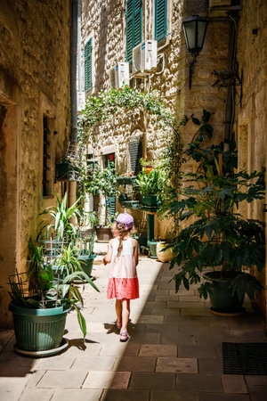 A narrow courtyard in the historic town of Kotor, Montenegro, with a little girl walking through. The presence of greenery and the child exploring the courtyard add a touch of life and tranquility to the sceneの写真素材