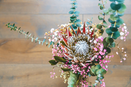 Top view a beautifully balanced floral arrangement, centered around a King Protea with striking spiky petals. The bouquet is surrounded by smaller, vibrant flowers in shades of pink and yellow, alongside lush greenery and textured eucalyptus leavesの写真素材