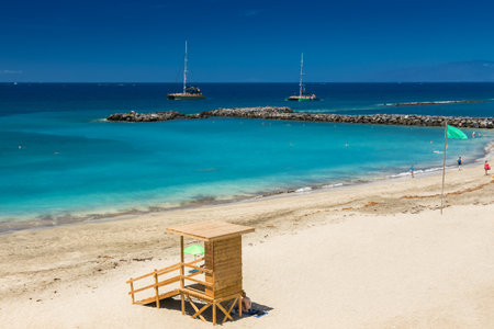 A scenic beach view at Playa del Duque, Tenerife, with golden sand and a lifeguard hut on the left side, displaying a green flag. Concept: beach holidays, leisure activities, and tourism in Tenerifeの写真素材