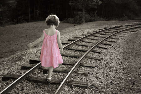 Colorized black and white with little girl in a pink dress walking on railroad trackの写真素材