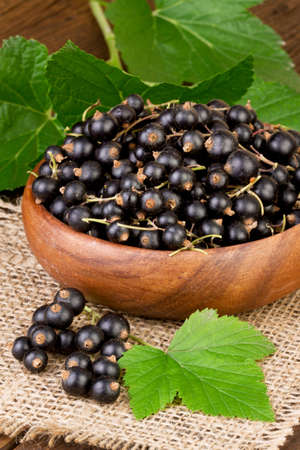 blackcurrant berries in wooden bowl on burlap jute backgroundの写真素材