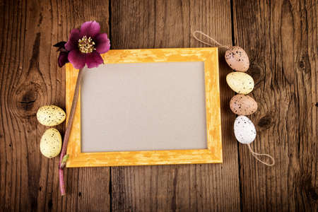 Easter greeting card with yellow picture frame on old wooden board. Top view with copy space.の写真素材