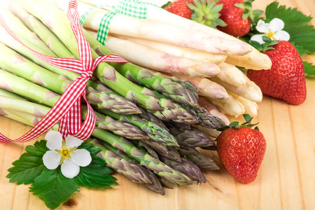 Asparagus closeup. Fresh green and white asparagus with strawberries on woodの写真素材