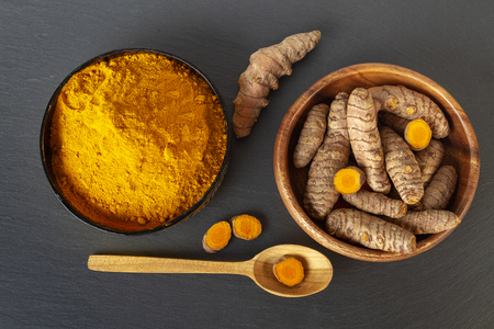 Turmeric roots and powder on gray slate background, overhead shotの写真素材