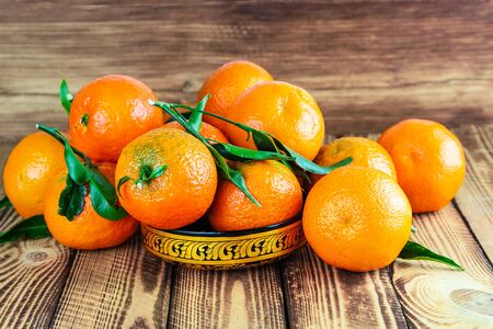 Fresh organic tangerines in beautiful gold bowl on old wooden backgroundの写真素材