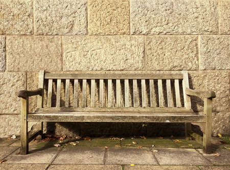 Empty bench in front of a stone wall with space for text.の写真素材