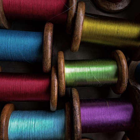 Vintage wooden spools with silk threads in a variety of colors including blue, red, green, yellow and purple.の写真素材
