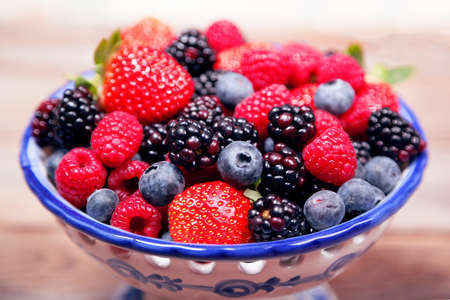 Mixed ripe sweet berries in a blue and white bowl  with shallow depth of field. Blueberries raspberries, strawberries and blackberries. With space for text.の写真素材