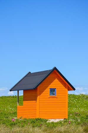 brightly colored orange beach house in the grass under a blue skyの写真素材