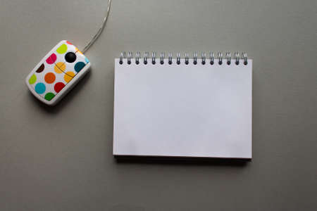 White computer mouse with color dots and spiral notebook on grey background. minimal style. top viewの写真素材