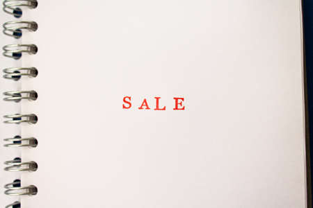 The red word sale stamped on a spiral notebook. Price reduction and promotion in trade and services concept photoの写真素材