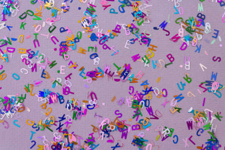 Multicolored sparkle glitter confetti letters on lilac for party or festive background. Holiday and fun conceptの写真素材