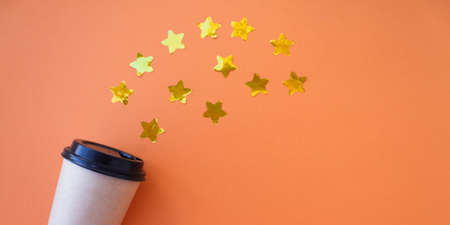 Banner Coffee to go concept. Disposable craft cup with black plastic cover on a trendy orange background with gold stars confetti. Place for text. Flat lay style. Top viewの写真素材